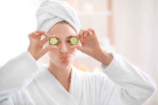 Young woman in bathrobe and with cucumber slices at home - Foto, imagen