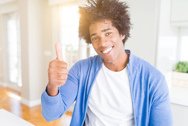African American man at home doing happy thumbs up gesture with hand. Approving expression looking at the camera showing success. - Photo, Image