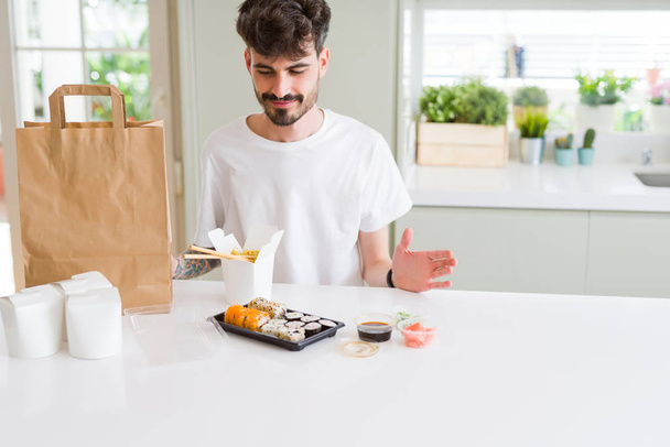 Νέος άνθρωπος που τρώει σούσι ασιατικό φαγητό και νουντλς με χρήση των εκλεκτικών στικ  - Φωτογραφία, εικόνα