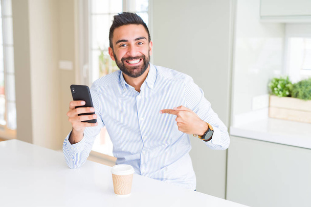 Yakışıklı İspanyol iş adamı kahve içme ve sürpriz yüz ile akıllı telefon kullanarak kendini parmak işaret - Fotoğraf, Görsel