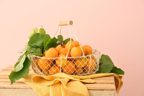 Корзина с вкусными спелыми абрикосами на деревянной коробке на цветном фоне
 - Фото, изображение