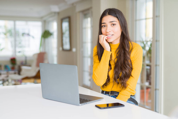 コンピュータのラップトップを使用している若い女性は、口を噛む爪に手でストレスと緊張を見ています。不安の問題. - 写真・画像