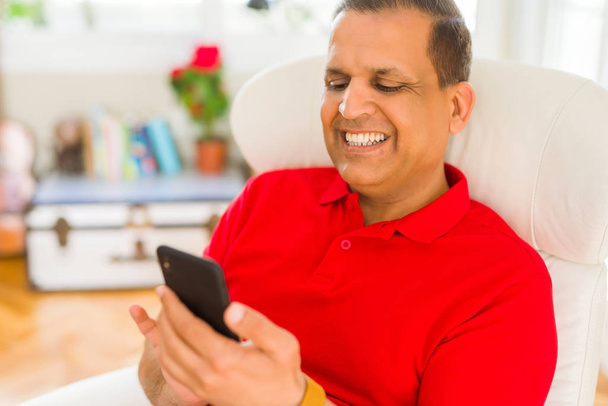 Muž středního věku s úsměvem veselá bílá pomocí smartphone sedí na gauči doma - Fotografie, Obrázek
