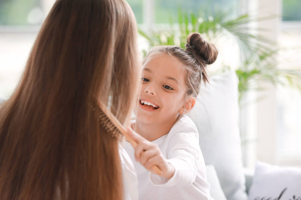 Little daughter doing hair of her  mother at home in morning - Фото, изображение