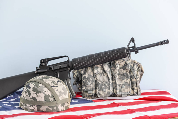 Военный шлем, жилет, штурмовая винтовка и флаг США на столе
 - Фото, изображение