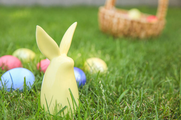 Keramický zajíček s barevnou velikonoční vajíčky na trávě venku - Fotografie, Obrázek