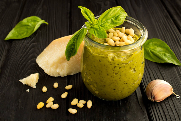 Sauce pesto in the glass jar and ingredients on the black  wooden background - Foto, Bild