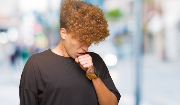 Mladý pohledný muž s afro vlasy, nosí černé tričko, pocit nevolnosti a kašle jako příznak nachlazení či zánět průdušek. Zdravotnické koncepce. - Fotografie, Obrázek
