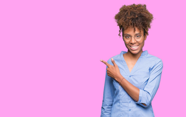 Γυναίκα όμορφη νεαρή αφρικανική αμερικανική επιχείρηση πέρα από το απομονωμένο υπόβαθρο χαρούμενα με ένα χαμόγελο του προσώπου δείχνει με το χέρι και δάχτυλο μέχρι την πλευρά με ευτυχισμένο και φυσική έκφραση στο πρόσωπό - Φωτογραφία, εικόνα