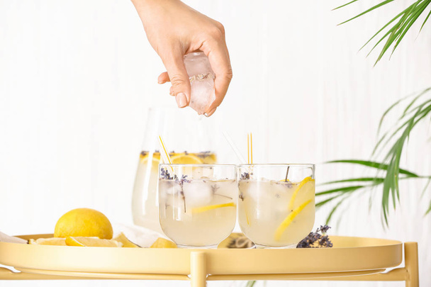 Woman dropping ice cubes into glass of lavender lemonade on table - Φωτογραφία, εικόνα