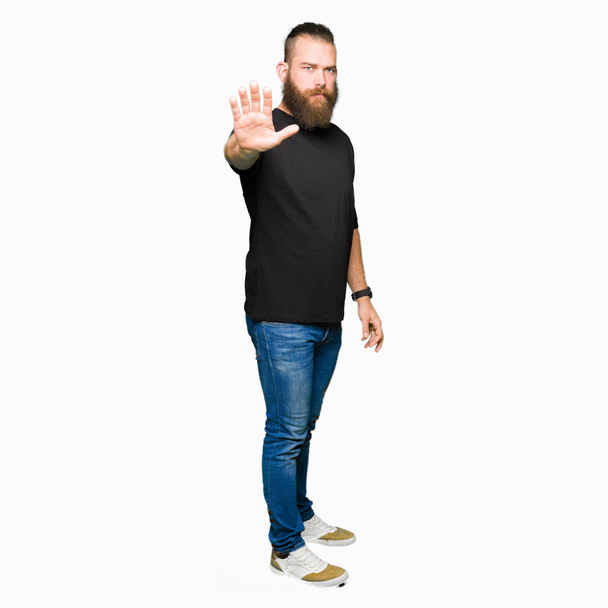 Young blond man wearing casual t-shirt doing stop sing with palm of the hand. Warning expression with negative and serious gesture on the face. - Photo, Image