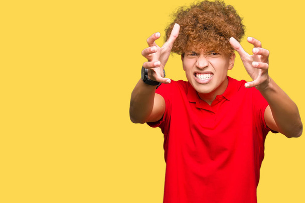 junger gutaussehender Mann mit Afro-Haaren trägt rotes T-Shirt und schreit frustriert vor Wut, Hände versuchen zu würgen, schreien verrückt - Foto, Bild