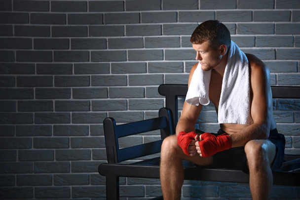 Strong male boxer sitting on bench against brick wall - Foto, Imagem
