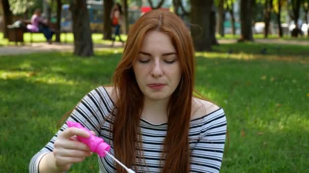 Red-haired girl blows soap bubbles in the park She smiling and laughing summer and happiness  - Πλάνα, βίντεο