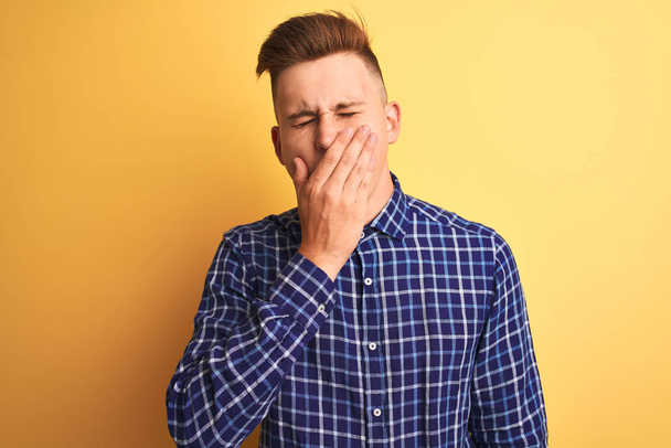Young handsome man wearing casual shirt standing over isolated yellow background bored yawning tired covering mouth with hand. Restless and sleepiness. - Photo, Image