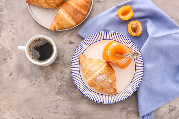 Jar with tasty apricot jam, croissants and coffee on grey table - Fotó, kép