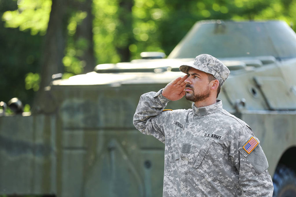 Saluting soldier in camouflage near armored fighting vehicle outdoors - Photo, Image