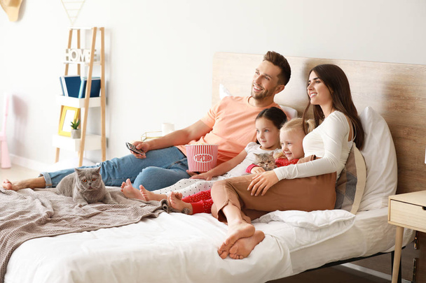 Famille heureuse avec des chats mignons regardant la télévision sur le lit à la maison
 - Photo, image