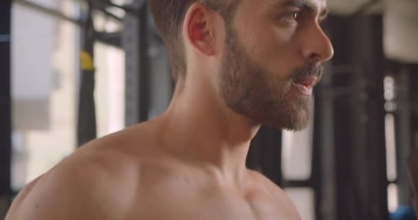 Closeup portrait of shirtless muscular caucasian man working out with dumbbells with effort standing in the gym indoors - Séquence, vidéo
