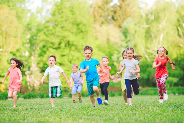 Sok különböző gyerekek, fiúk és lányok futnak a parkban napsütéses nyári napon alkalmi ruhák. - Fotó, kép
