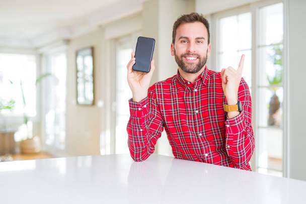 Handsome man showing smartphone screen very happy pointing with hand and finger to the side - Photo, Image
