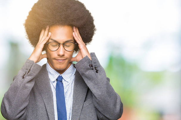 Νεαρός αφρικανική αμερικανική επιχείρηση άνθρωπος με τα άφρο μαλλιά που φοράει γυαλιά με το χέρι στο κεφάλι για πόνο στο κεφάλι, επειδή το άγχος. Υποφέρουν ημικρανία. - Φωτογραφία, εικόνα