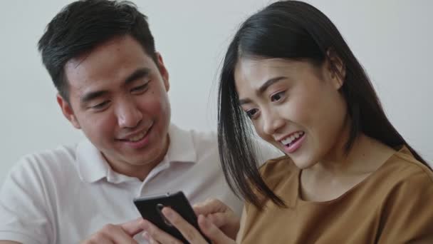 Lassú mozgás: közelről fiatal ázsiai pár segítségével mobiltelefon böngészés szociális média kommunikáció és vásárlás online ülve a kanapén otthon. - Felvétel, videó
