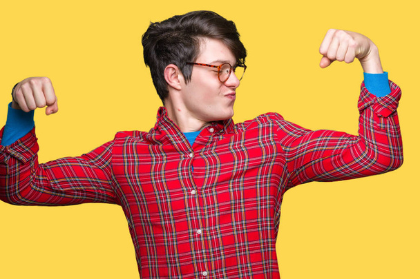Mladý pohledný muž nosí brýle izolované pozadí ukazuje svaly paže s úsměvem hrdá. Fitness koncept. - Fotografie, Obrázek