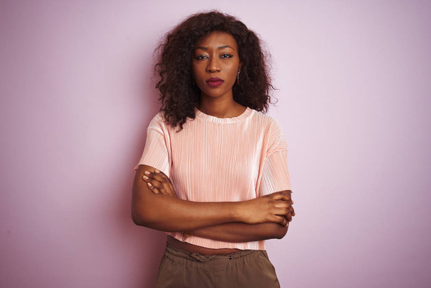 Молодая африканская американка в футболке стоящая на изолированном розовом фоне скептически и нервно, неодобряющее выражение лица со скрещенными руками. Отрицательное лицо
. - Фото, изображение