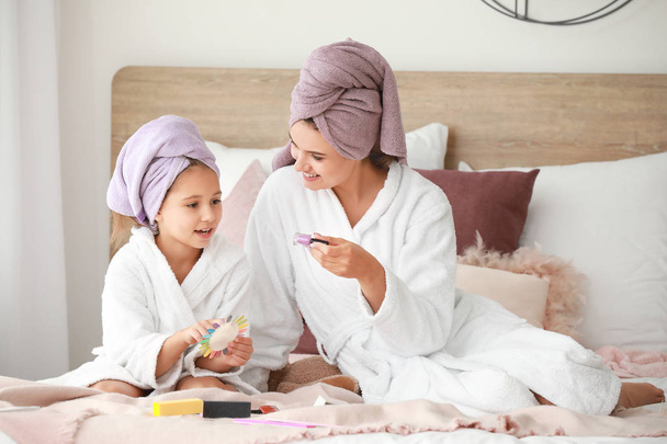 Mother and her little daughter in bathrobes manicuring nails in bedroom - Fotoğraf, Görsel
