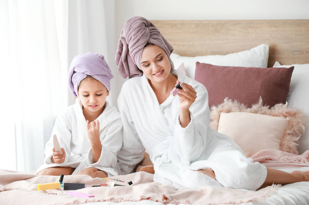 Mother and her little daughter in bathrobes manicuring nails in bedroom - Photo, Image