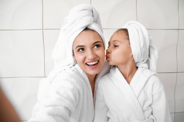 Mother and her little daughter in bathrobes taking selfie against white background - Photo, Image