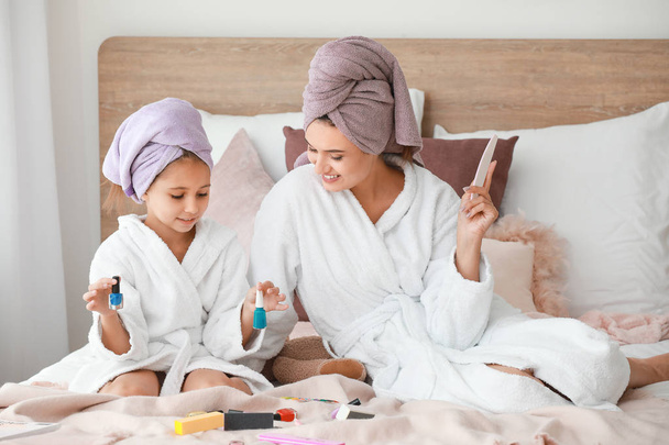Moeder en haar kleine dochter in badjassen manicuring nagels in de slaapkamer - Foto, afbeelding