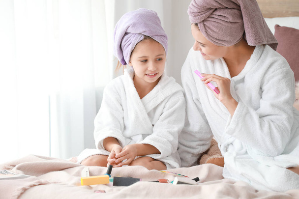 Mother and her little daughter in bathrobes manicuring nails in bedroom - Фото, зображення