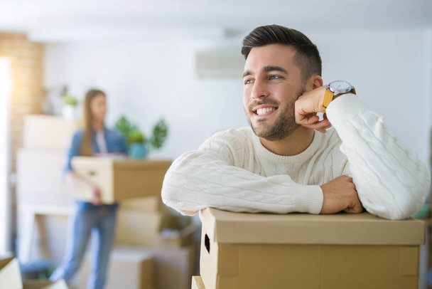 Young couple moving to a new home, handsome man smiling leaning on cardboard boxes - Fotoğraf, Görsel
