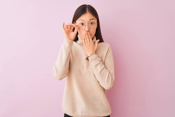 Jonge Chinese vrouw dragen coltrui trui en glazen over geïsoleerde roze achtergrond cover mond met de hand geschokt met schaamte voor fout, uitdrukking van angst, bang in stilte, geheime concept - Foto, afbeelding
