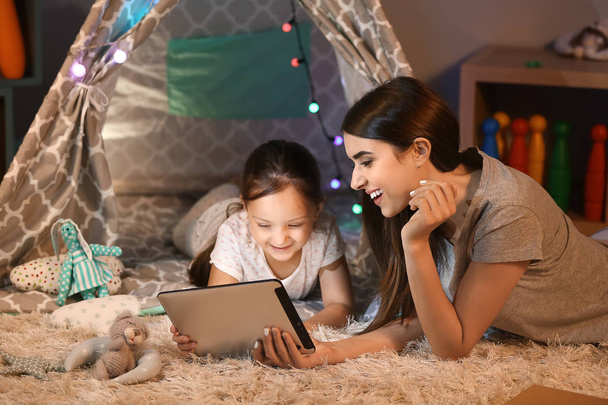 Mãe e sua filhinha com computador tablet em casa à noite
 - Foto, Imagem
