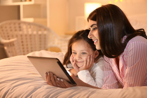 Woman and her cute little daughter with tablet computer in bedroom - Foto, imagen