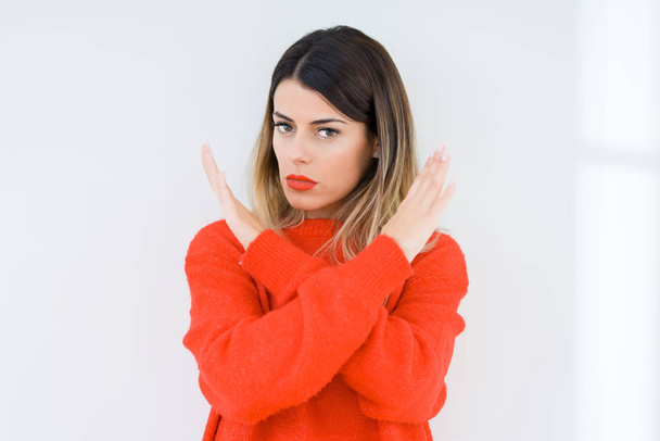 Mujer joven con suéter rojo casual sobre fondo aislado Expresión de rechazo cruzando brazos haciendo signo negativo, cara enojada
 - Foto, imagen