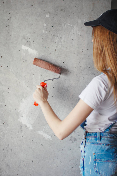 Selective focus at painting roller in young Caucasian woman hand in front of a reparing new wall in a room. - Fotografie, Obrázek