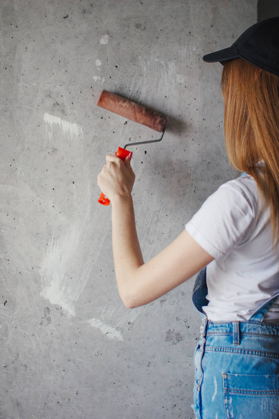 Selective focus at painting roller in young Caucasian woman hand in front of a reparing new wall in a room. - Foto, imagen