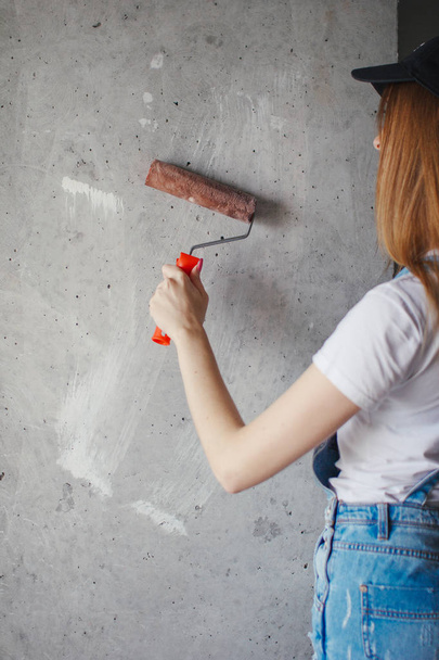 Selective focus at painting roller in young Caucasian woman hand in front of a reparing new wall in a room. - Фото, зображення