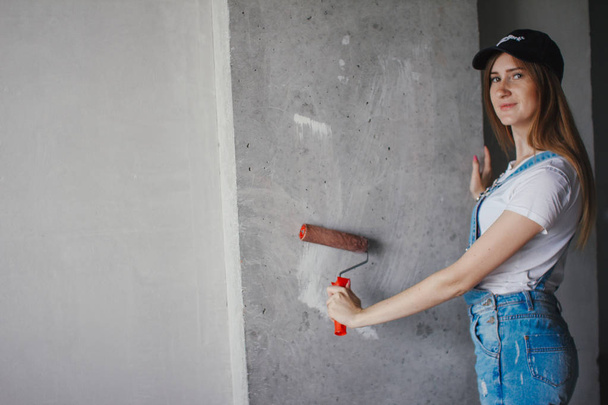 Selective focus at painting roller in young Caucasian woman hand in front of a reparing new wall in a room. - Fotografie, Obrázek
