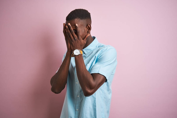 Mavi rahat gömlek giyen Afro-amerikan adam ağlarken elleri ile yüz kapsayan üzgün ifade ile izole pembe arka plan üzerinde duran. Depresyon kavramı. - Fotoğraf, Görsel