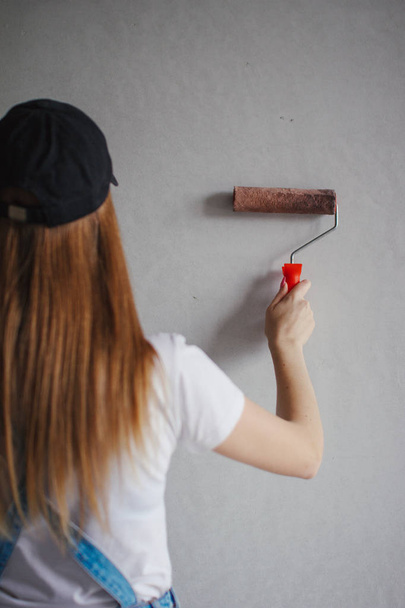Selective focus at painting roller in young Caucasian woman hand in front of a reparing new wall in a room. - Valokuva, kuva