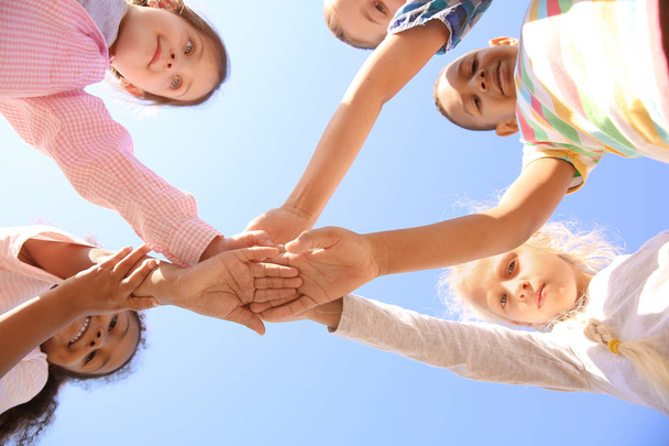 Lindos niños pequeños poniendo las manos juntas al aire libre, vista inferior
 - Foto, Imagen