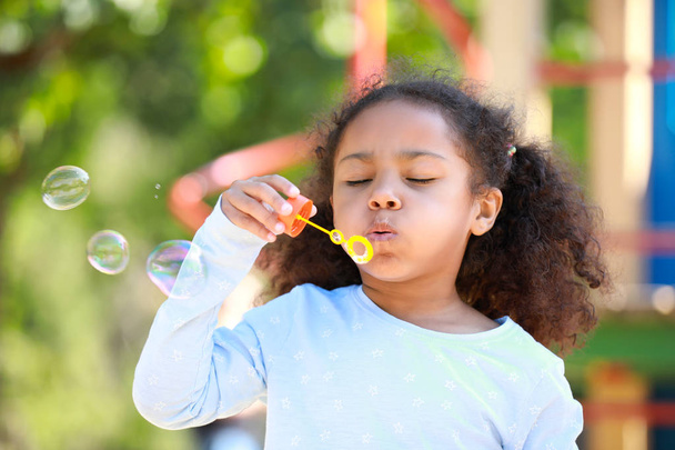Schattig Afrikaans-Amerikaans meisje blazen zeepbellen buitenshuis - Foto, afbeelding