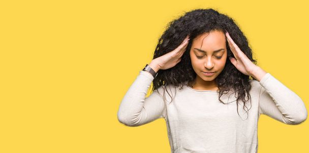 junge schöne Mädchen mit lockigem Haar trägt lässigen Pullover mit der Hand auf dem Kopf für Schmerzen im Kopf, weil Stress. Migräne. - Foto, Bild