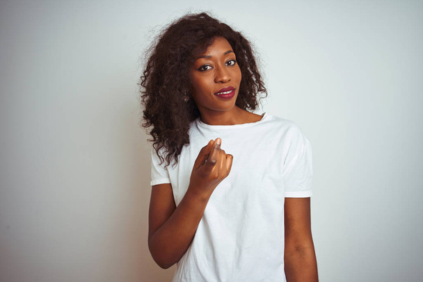 Joven mujer afroamericana vistiendo camiseta de pie sobre fondo blanco aislado Beckoning ven aquí gesto con la mano invitando a la bienvenida feliz y sonriente
 - Foto, imagen