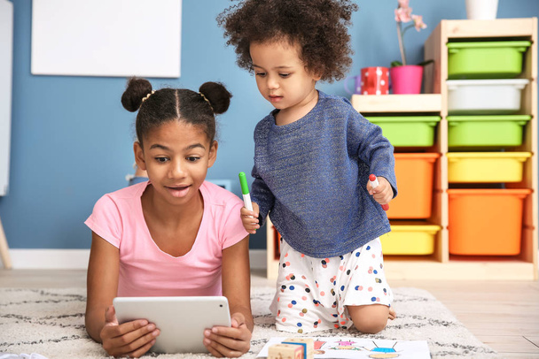 Cute African-American girl with tablet computer watching cartoons at home - Foto, afbeelding